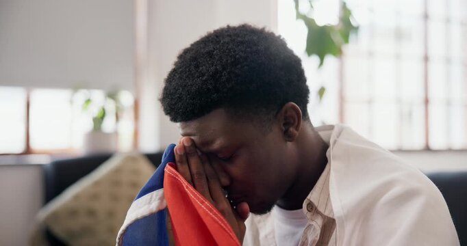 Disappointed, flag and black man watching tv in home, sports competition and upset for match game results. Live streaming, supporter and sad for tournament loss in lounge, frustrated and team failure