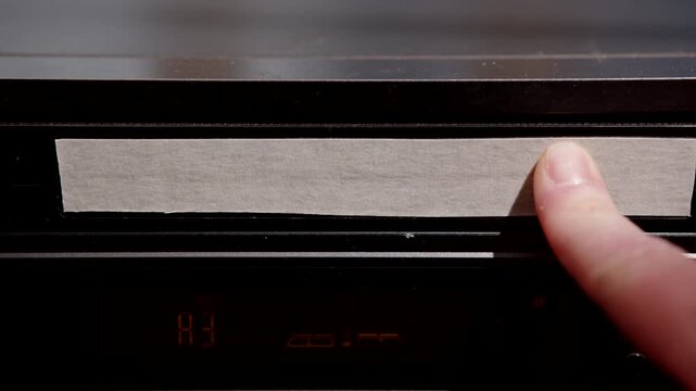 Woman's hand inserts video cassette into VCR slot close-up