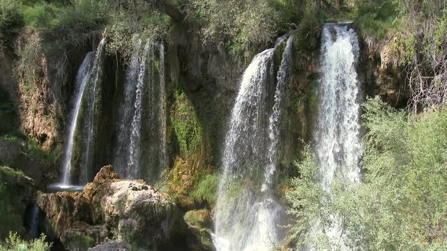 Sunny view of Sızır Waterfall in Sivas, Turkey, showing cascading streams and bright river flow. Fixed camera captures green valley, rocks, and sparkling water in a calm natural atmosphere.