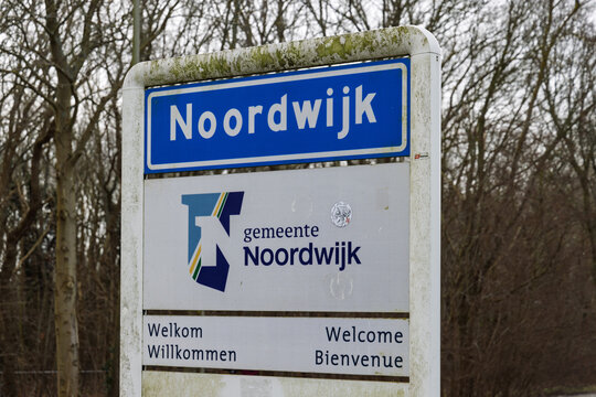 Close-up of the Noordwijk city entrance sign with the official municipal logo and multilingual welcome text, set against a background of trees. Noordwijk Netherlands, 24 february 2026