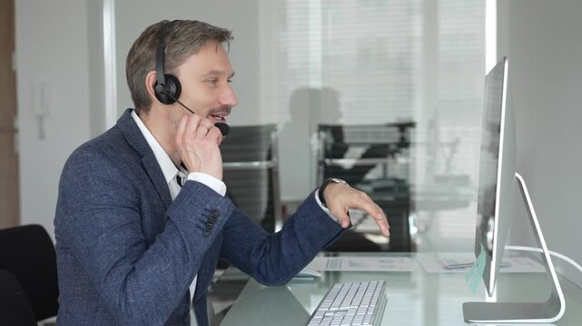 Male call center agent wearing headset providing online customer support, consulting client on headset video call. Business people concept