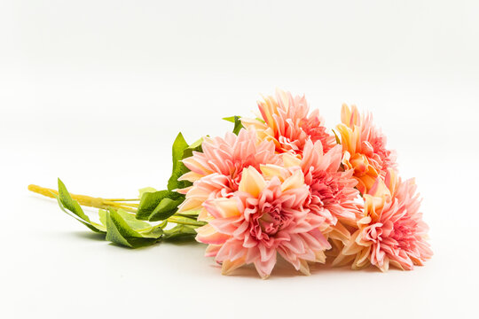 A high-quality studio shot of a vibrant artificial peach dahlia bouquet featuring multiple blooming flower heads and green leaves.
