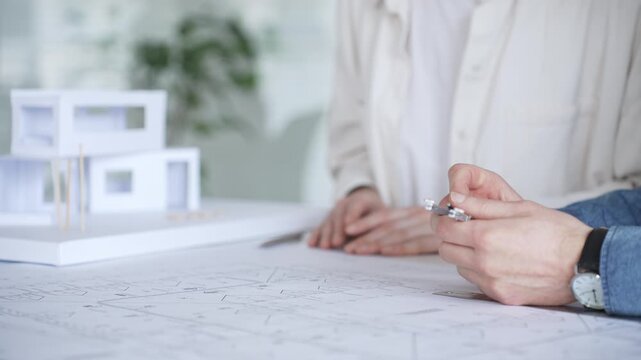 Architects collaborating on blueprint plans, discussing engineering details and project designs, planning construction development with a laptop in a modern office environment