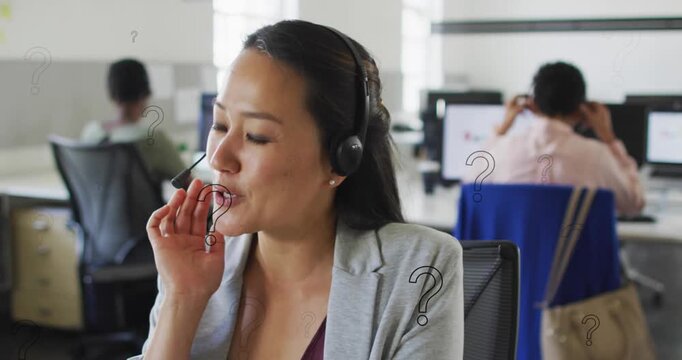 Animation of question mark symbols over asian woman talking over headphones at office