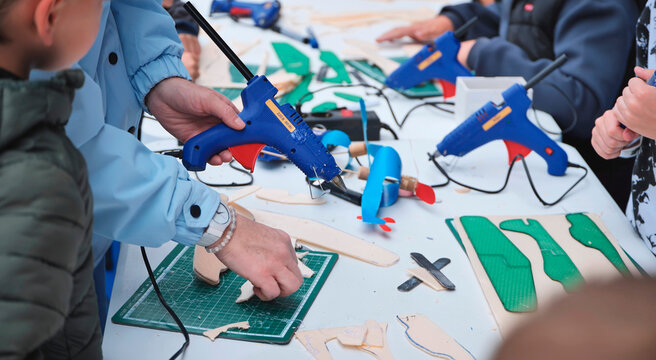 Adults and children crafting model airplanes with glue guns at a workshop