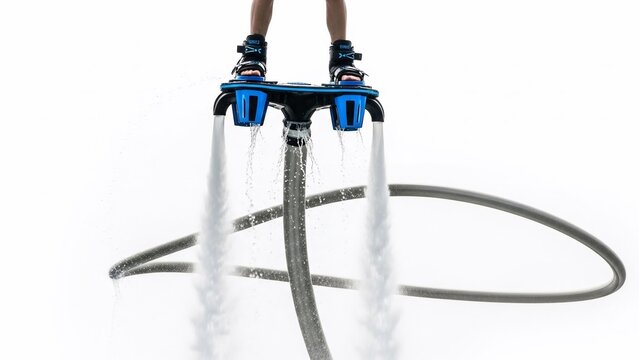 A person's feet strapped into a blue and black flyboard device with powerful water jets propelling water downwards on a white background.