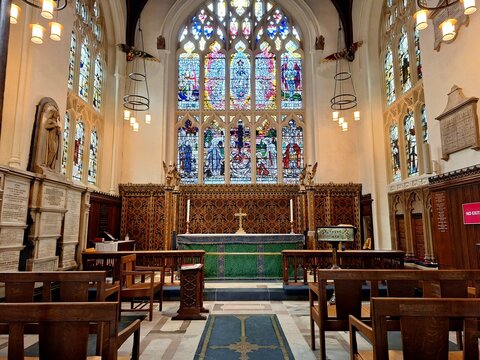 The richly adorned high altar of Leicester Cathedral is framed by intricate Gothic arches and vibrant stained glass windows depicting biblical figures.