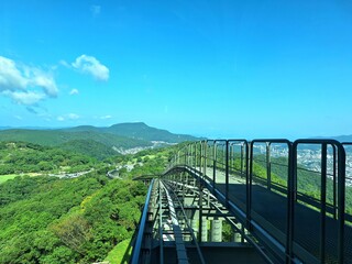 Fototapeta premium A dynamic uphill perspective from the Mount Inasa ropeway captures the sweeping green hills of Nagasaki unfolding below.