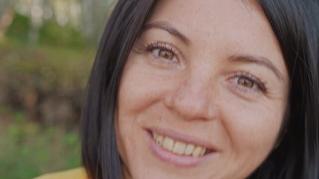 White woman camping closeup speaks to camera with playful expressions and bright eyes, sunglasses perched on head, relaxed yellow jacket, birch backdrop, candid storyteller sharing foraging tips