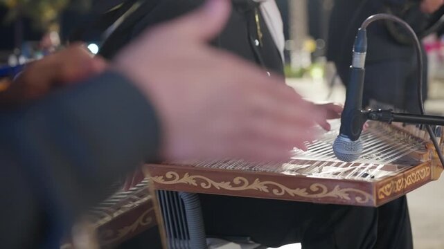 Woman playing traditional qanun instrument with musicians performing on darbuqa drum at outdoor evening event