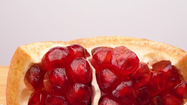 A close-up shot of a halved pomegranate, with its bright red seeds (arils) clearly visible, spinning smoothly on a rustic wooden table surface. Healthy food concept.