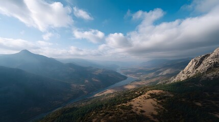 Obraz premium Panoramic view of a vast mountain valley with a river flowing through under a dramatic sky with clouds and hints of autumn foliage