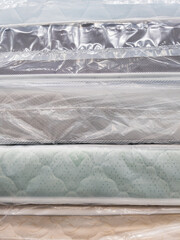 Naklejka premium Stack of new mattresses in plastic wrap, various fabric covers visible from the side