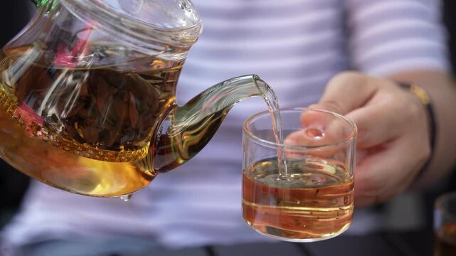 Herbal green tea is poured from a teapot into a glass cup on the table.