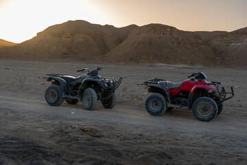 two quad bikes parked in a vast rocky desert landscape during golden hour sunset with beautiful mountains in the background for adventure travel and safari in Africa © marekfromrzeszow