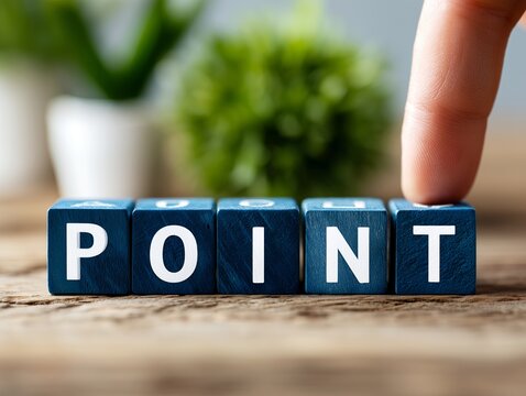 木製の机に並んだ青いブロックのPOINTという文字を指で押さえるビジネスマンの手