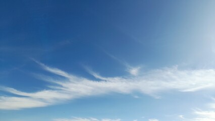 Obraz premium Wispy white cirrus clouds on a clear bright blue sky background on a sunny day.