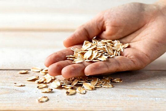 Hand holding a handful of organic oat flakes over a wooden table, healthy breakfast concept.