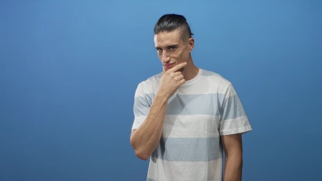 Man with hand on chin touching his chin in studio wearing striped tshirt against a blue backdrop; thoughtful.