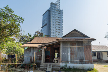 Fototapeta premium The Life of an Average Poor A modest tin shelter in the foreground contrasts sharply with a towering modern skyscraper behind it, highlighting the gap between everyday struggle and rapid urban growth.