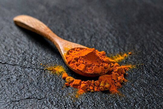 Curcumin powder in a rustic wooden spoon isolated, aromatic Indian spice macro shot.