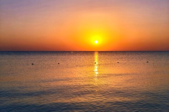 Rising vivid colorful sun, calm ocean surface with small waves under the morining sky. Distant vivid sky, sea and the sunrise. Sun, clouds and water with the buoys, landscape travel photography. 