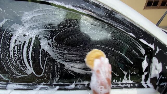Hand holding sponge with soap foam washing white car