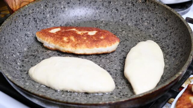 A close-up of potato pies being fried in a frying pan. The cook flips the pies with a fork.