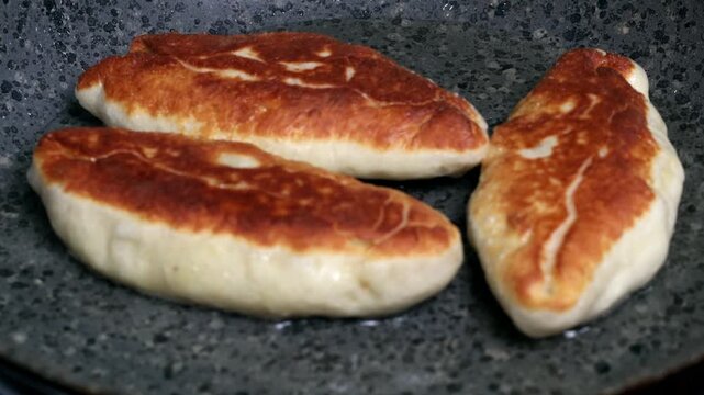 A close-up of potato pies being fried in a frying pan. The cook flips the pies with a fork.