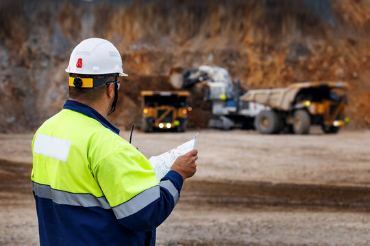 Engineer worker supervisor in high visibility jacket and helmet reviewing plans and work of truck at open pit mine for safety briefing