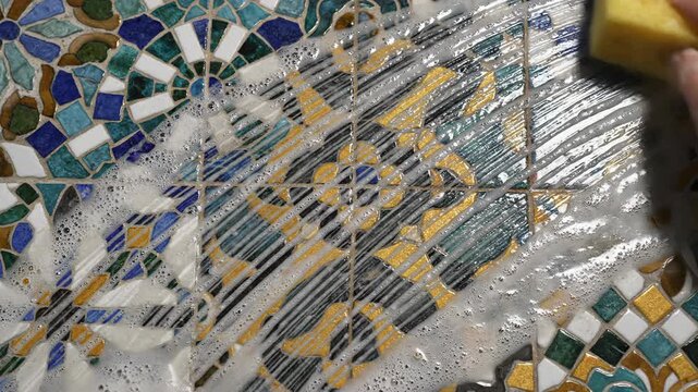 Hand cleaning intricate mosaic tiles with soapy sponge, detailed pattern surface, domestic cleaning, household chores