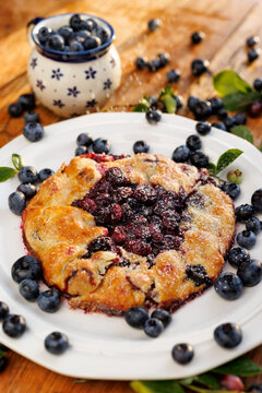 Bluebbery galette on a white ceramic plate on a wooden table, close up view. Delicious homemade pastry