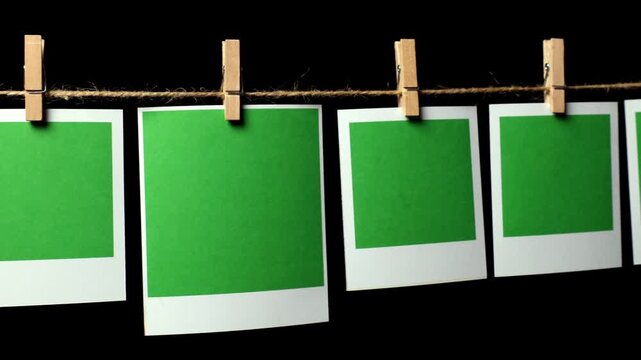 A row of green pieces of paper with a white frame against a black background. The camera pans from left to right, looking down the row of papers. Space for text.
