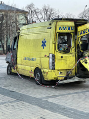Damaged and burned yellow ambulance displayed outdoors on a city square, with historic European architecture visible in the background. © Yuliia Litvinova