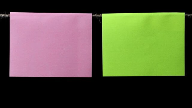 Two square pieces of pink and green paper hang on a thin rope against a black background. Space for text.