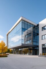 Fototapeta premium Corner cantilever glass lobby of modern office building with open plaza, autumn trees and bright clear blue sky