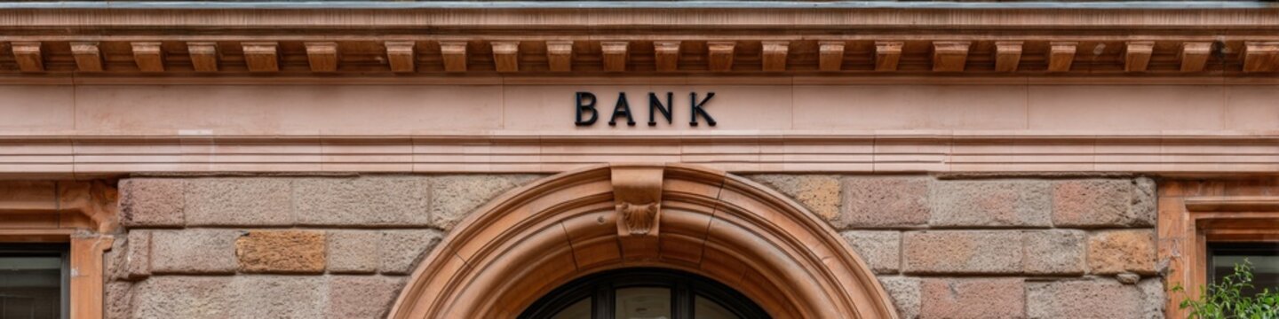 Bank sandstone facade with engraved signage arched doorway rusticated stonework and decorative entablature historic financial building