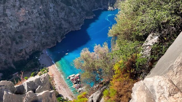 Butterfly Valley beach and turquoise cove seen through rocky cliffs and olive trees from a dramatic high vantage point, Fethiye, Turkey