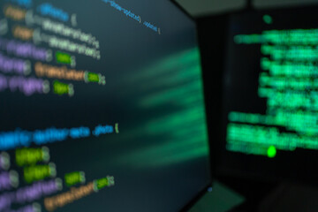 Dark room glows with green code on two screens.  Code scrolls in vibrant syntax, hinting at deep technical work © KANGWANS