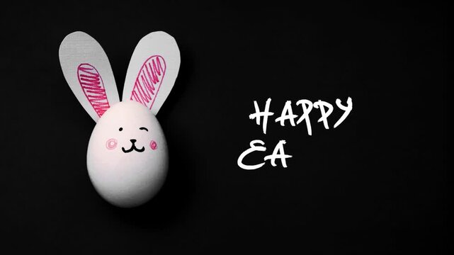 Horizontal 4K video. Top view. Stop motion animation. White chicken egg with paper rabbit ears and cute bunny face on black background. Flat lay. Hand written text Happy Easter. Farm food on table
