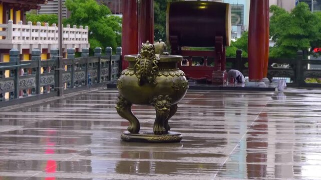 A massive bronze color offering bowl stands on curved legs near the entrance to Viet Nam Quoc Tu Pagoda (Vietnamese National Pagoda) in Saigon (Ho Chi Minh City) during the rain