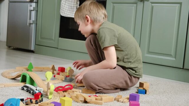 Cute little blonde child boy sitting on the floor playing with wooden toy train. Toddler kid plays railway. Made of natural materials. Birthday gift. Preschool employment. Brain, coordination exercise