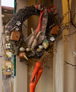 Rustic twig wreath decorated with a fabric bunny, miniature birdhouses, speckled eggs, quail eggs, moss, and hanging carrots. Whimsical Easter wall decor for spring interiors, holiday styling, handmad