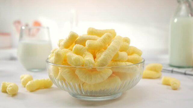 Airy corn puffs in glass bowl, breakfast style setting with milk bottle and honey jar, clean white background