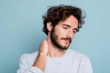 Fototapeta premium Young caucasian male with sore neck and pained expression touching neck against blue background