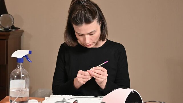 Young woman pushing back cuticles with wooden stick at home