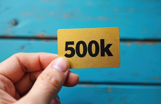 Hand holds golden card with 500k text. Symbolizes reaching 500000 followers or subscribers. Celebrates major business milestone or sales target. Commemorates important business growth.