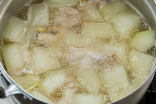 Clear soup with winter melon and chicken boiling in a pot, light broth simmering with steam, showing home-style Thai cooking process