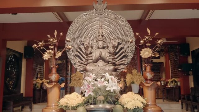 Incredible ornate statue of one thousand arm Buddha Bodhisattva of compassion Avalokiteshvara is offered white and pink lilly and chrysanthemum flowers with golden color vases in front of it