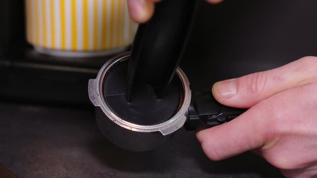 Close-up of a barista tempering freshly ground coffee with a tempera in a coffee shop. The process of making espresso. Footage of barista tamping coffee in pitcher of a barista crafting an Americano. 